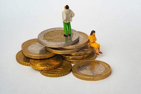 Zwei Plastikfiguren, eine Frau und ein Mann, platziert auf einem Stapel Geldmünzen.